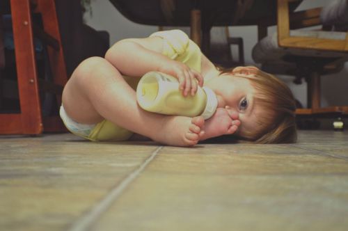 Ребенок пьет из бутылочки лежа на полу