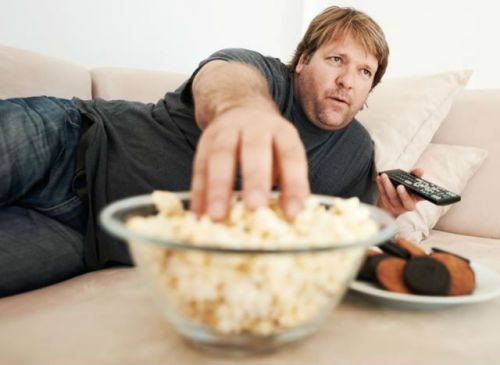 Мужчина перед телевизором ест попкорн